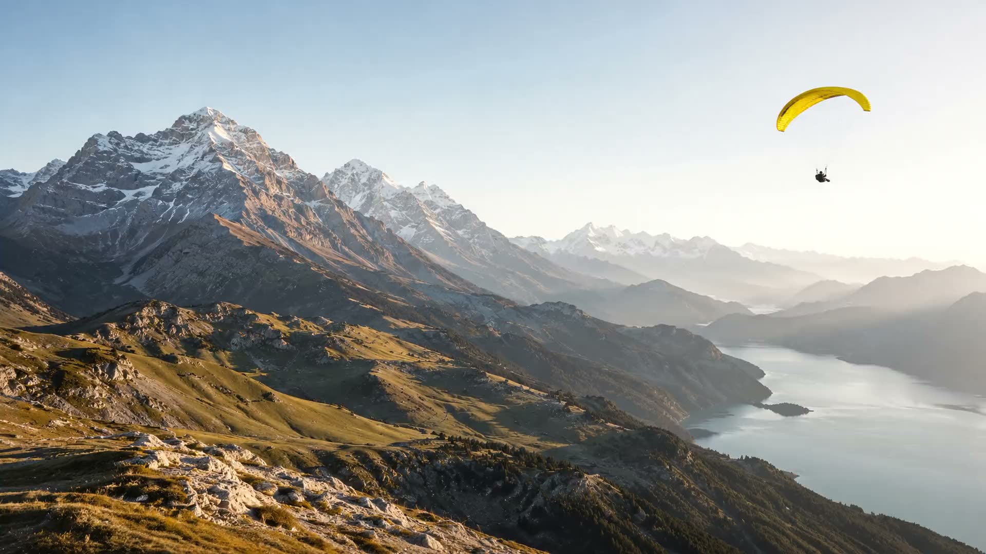 Paraglider with a yellow wing above golden alpine peaks at first light